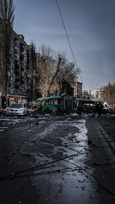 A photograph depicting the aftermath of a collision involving a green and black double-decker bus and a fallen tree in an urban residential area. The scene shows the bus tipped onto its side with visible structural damage, surrounded by debris including broken glass, scattered tiles, and blackened, burnt materials on the wet pavement. Nearby, damaged cars and a fallen tree leaning against power lines are visible. Multi-storey apartment buildings are in the background, with leafless trees lining the street under cloudy skies. The picture captures the chaos caused on the street during a home relocation or moving process, highlighting the importance of careful planning and secure transport methods as emphasized by Man with Van Camberwell.